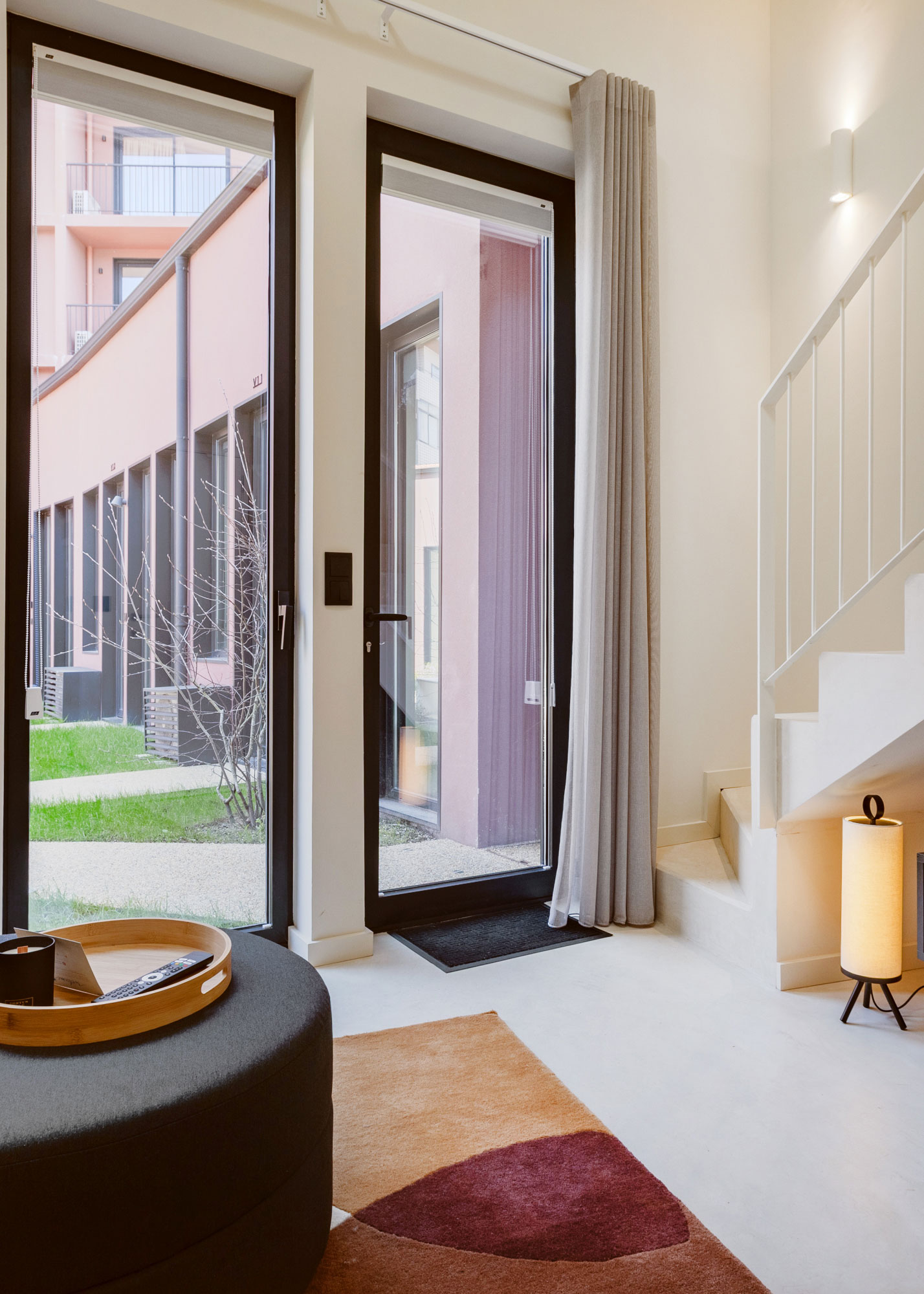 Sala de estar com portas de vidro de correr, vista para pátio interior com fachadas coloridas e pouf circular escuro — projeto de alojamento local no Porto